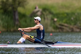 Jacob Plihal in a USA uniform, as he is mid-stroke while rowing across a river.