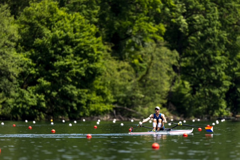 Jacob Plihal rowing down a river marked by orange and white buoys. 