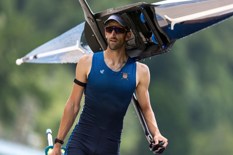 Jacob Plihal carries his boat over his head with one hand while his other holds an oar. 