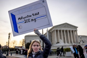 A protestor holding a sign that depicts a drawing of a box of Mifepristone pills.