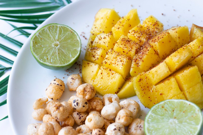 Cut mangos, limes, and AshaPop popped water lily seeds lie on a plate.