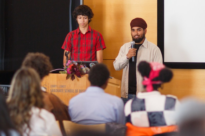 A person speaking into a microphone at the Summer Youth Employment Program ceremony.