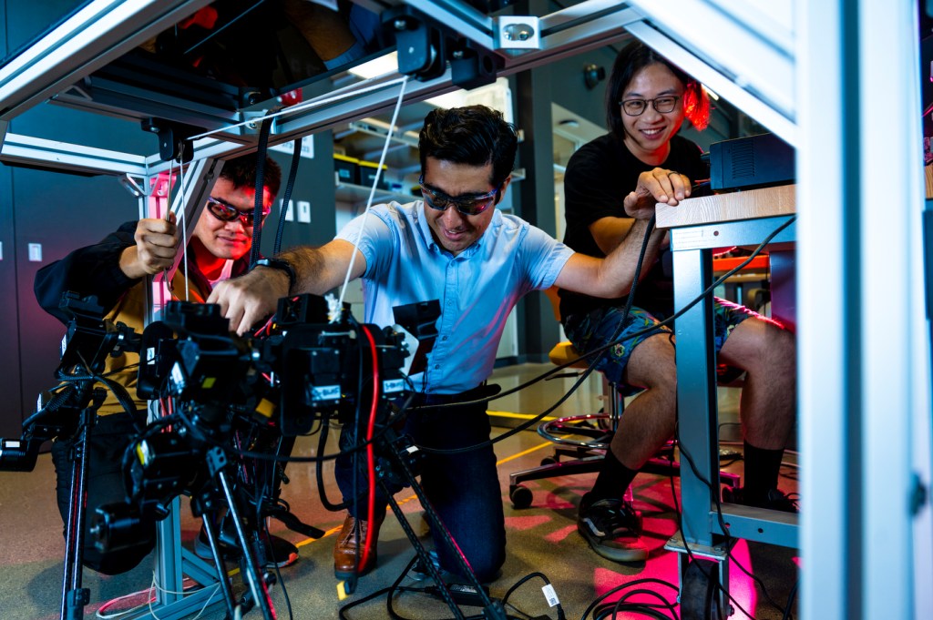 Three people sit around a robotics project while testing it.