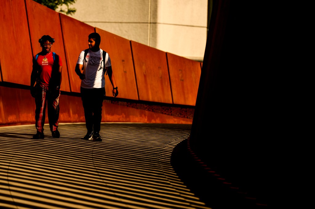 Two people walk across a bridge on a sunny day outside.