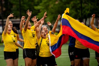 Soccer players wave a Colombia flag and cheer with their hands in the air on a soccer field.