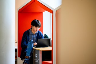 A Northeastern University student sits in a bright red booth working on their laptop.