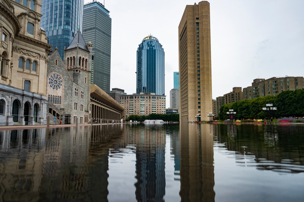 City skyscrapers reflect onto a pond on a sunny day.