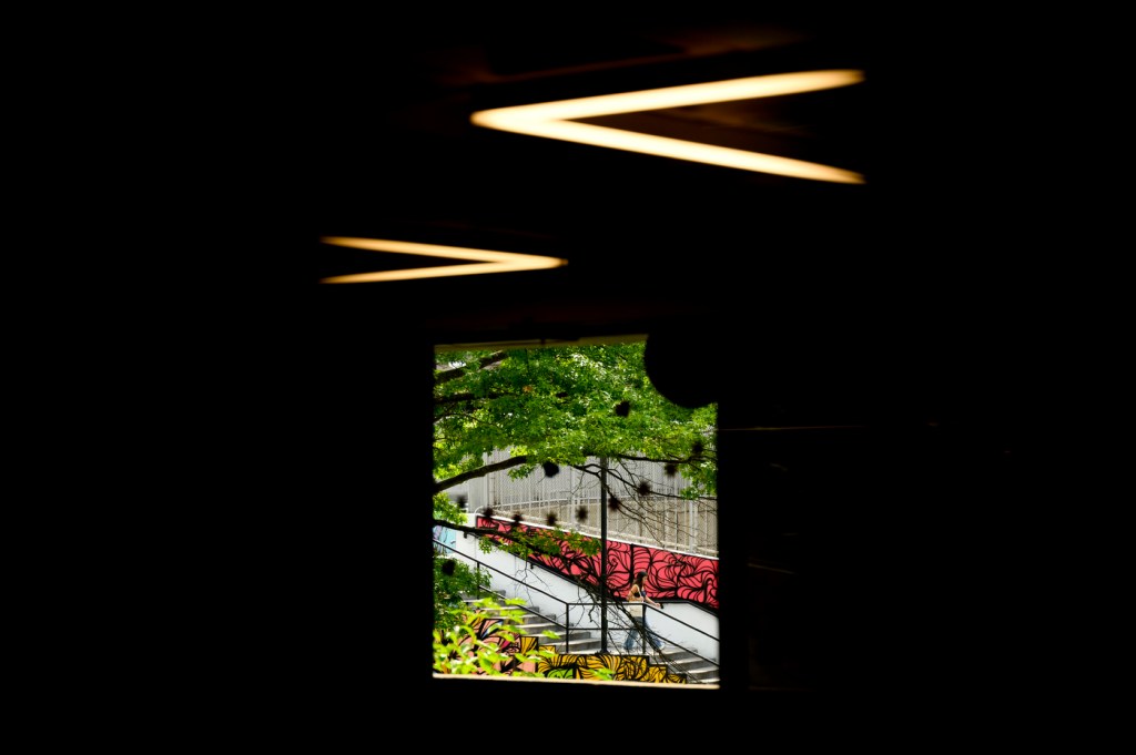 A person walks past a multi-colored mural as they head toward cement stairs outside on a cloudy day.