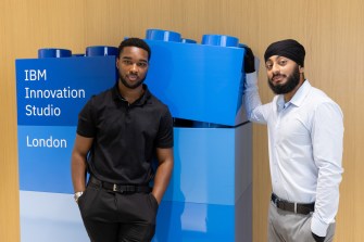 Two students posing in front of large blue lego blocks that say 'IBM Innovation Lab' on them.