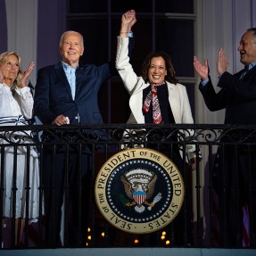Joe Biden and Kamala Harris stand on a balcony raising their hands together.