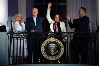 Joe Biden and Kamala Harris stand on a balcony raising their hands together.