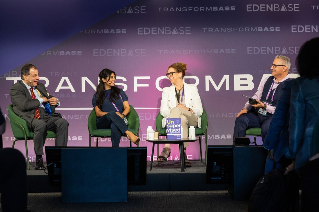 Four people sit together on a stage in front of a purple background with white text: "TransformBase".