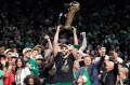 Jayson Tatum holding up a championship trophy while surrounded by other members of the Boston Celtics team.