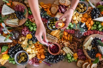 An overhead shot of a bountiful cheeseboard including many kinds of cheese, grapes, olives, dried fruit, crackers, dried meats, and jams.
