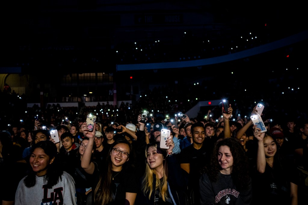 Students holding up their phones with their flashlights on in a darkened arena.