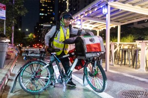 An immigrant walks his bike that has a Mexican flag on it across a street.