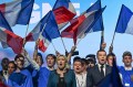 While waving the French flag, Marine Le Pen sings next to Jordan Bardella while surrounded by National Rally party members.