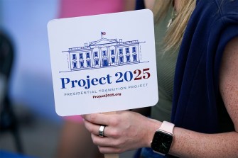 Person holds up a Project 2025 sign with a drawing of the White House on it.