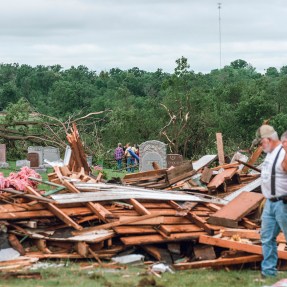 People looking at the rubble of a house from a tornado's destruction.
