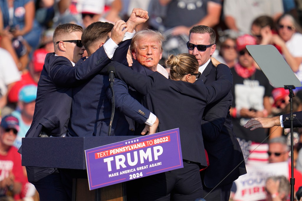 Former President Donald Trump raises his fist in the air as he is surrounded by Secret Service agents after a shooting at the Butler Boarding House.