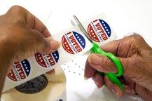 A person cutting up a sheet of I Voted stickers.