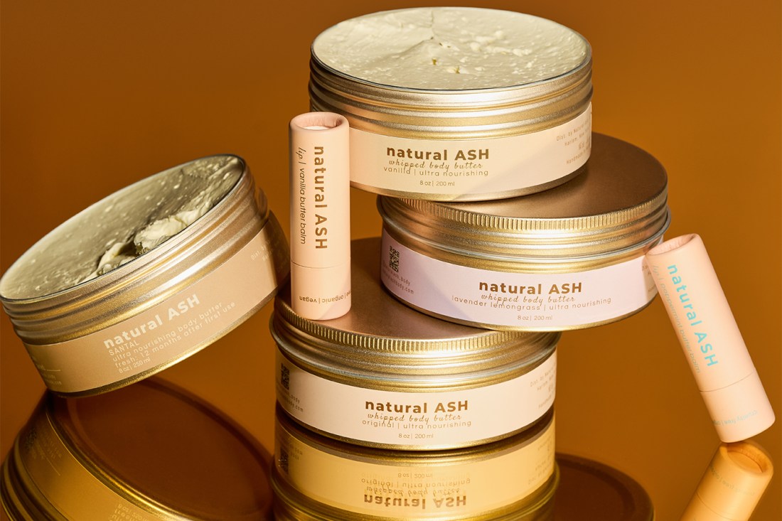 A pile of Natural Ash products, including their body butters and balms, are stacked on top of each other to display their labels.