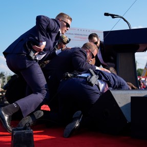 Secret service agents pushing Trump to the ground at his rally during his assassination attempt. One agent is in motion, hand on their gun.