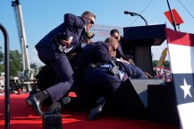 Secret service agents pushing Trump to the ground at his rally during his assassination attempt. One agent is in motion, hand on their gun.