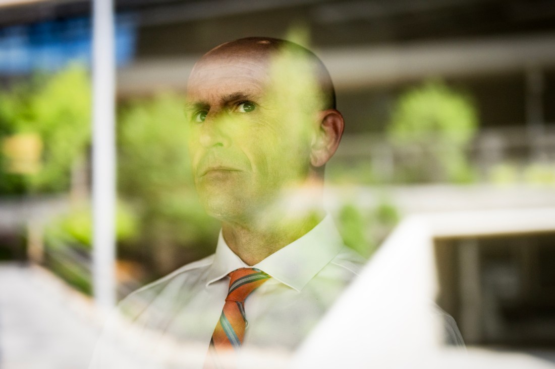 Jacob Stowell, Northeastern associate professor of criminology and criminal justice,  poses behind a reflective window for a portrait.