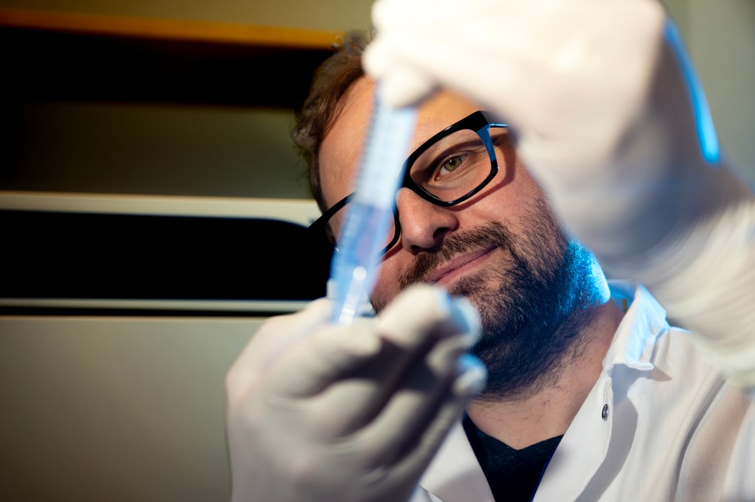 Nick Takacs examines a syringe with liquid in it in the lab.