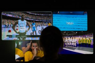 The silhouette of a person sitting in front of a multiview screen of Olympics events.