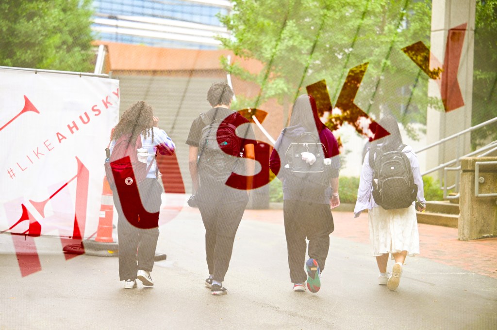 Four people walk side by side with backpacks, a bold graphic of red text reading "HUSKY" overlaid on the scene.