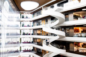 A spacious modern atrium with a striking spiral staircase, glass walls, and multiple floors featuring open workspaces and seating areas.