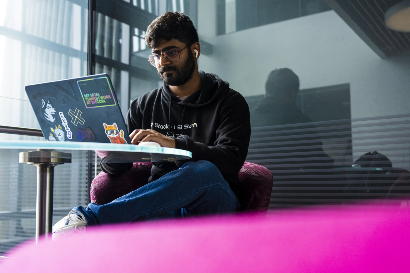 A person in a black hoodie and jeans works on his laptop.