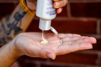 A person squeezing a bottle of sunscreen into their hand.