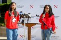 Two students wearing red Northeastern branded sweatshirts speaking into microphones at Oakland Press Conference.