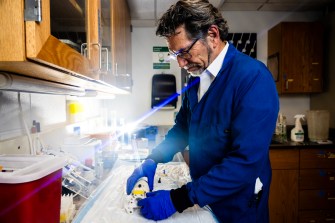 Craig Ferris working in a lab wearing a blue lab coat, safety goggles, and blue gloves.