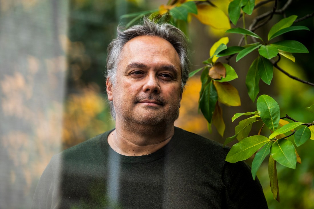 Carlos Cuevas, a professor of criminology, stands in an outdoor environment, with a branch of large green leaves over his left shoulder.