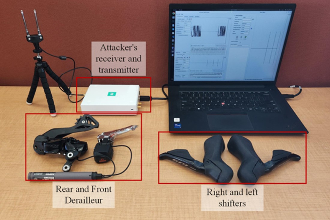 A laptop on a desk next to a receiver and transmitter, derailleurs, and bike shifters. 