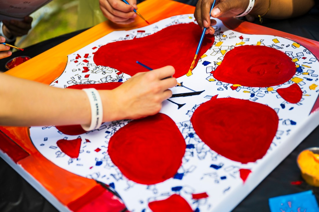 People paint a red paw print on a multi-colored canvas.