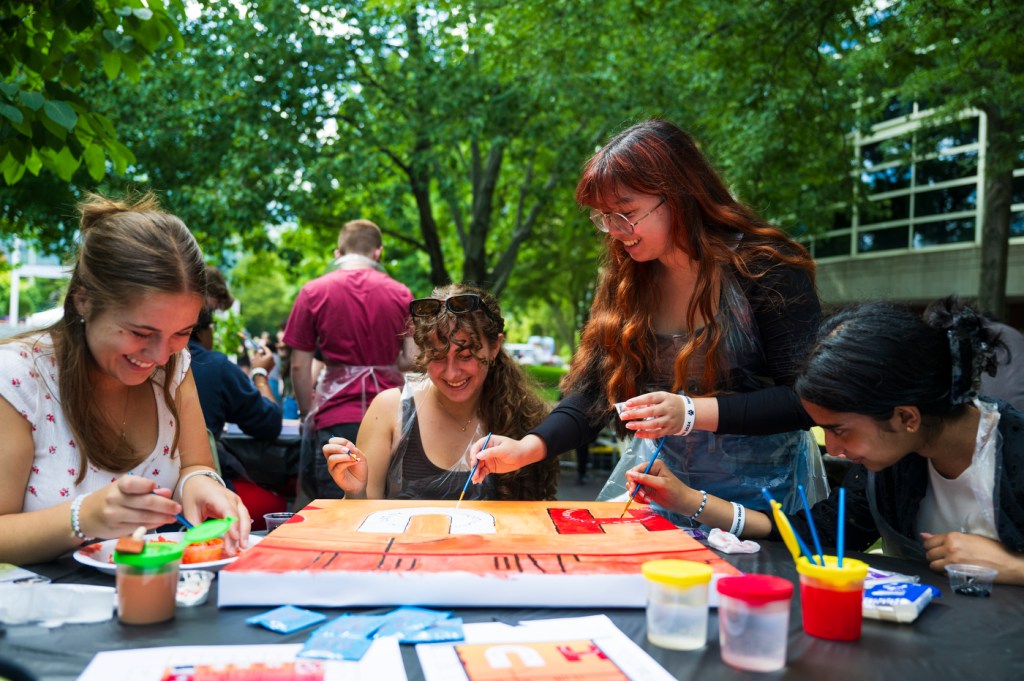 A group of people paint together outside on a sunny day.