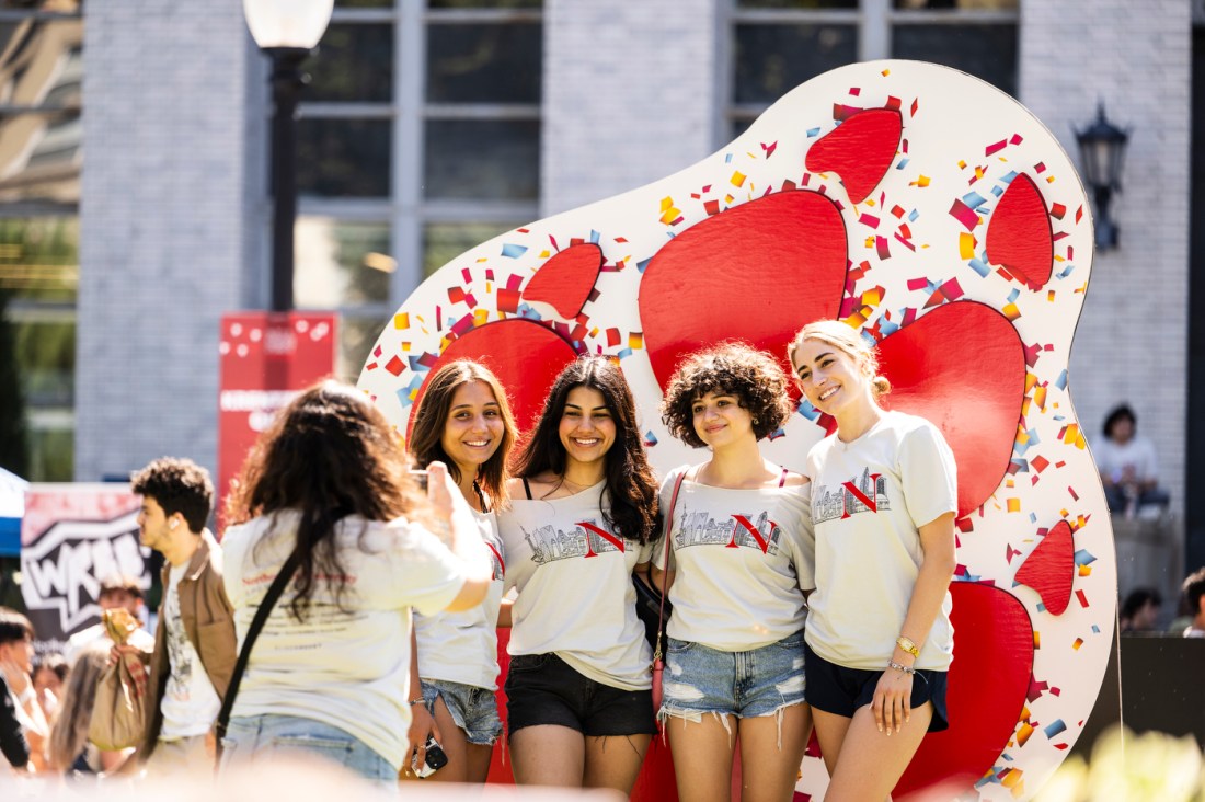 Four people pose for a photo in front of a large, red paw print over a white background.