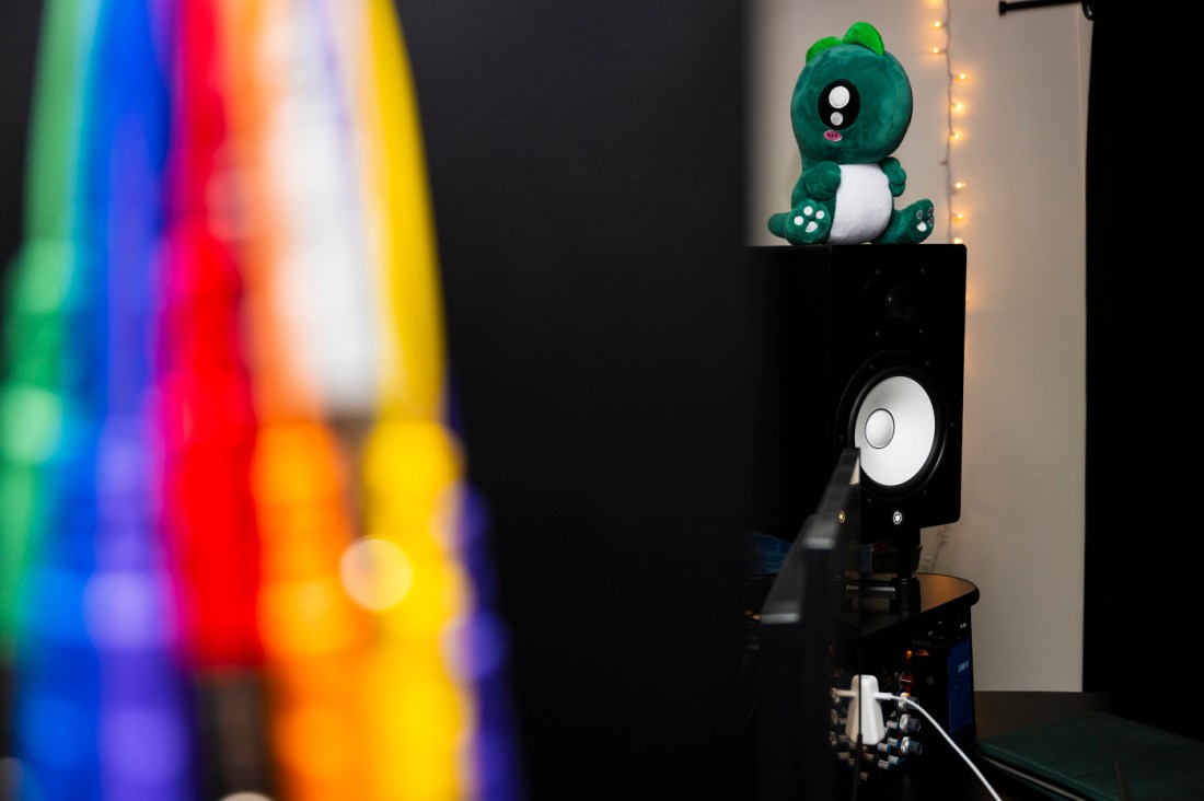 A green plush dinosaur on top of a computer monitor in the recording studio. 