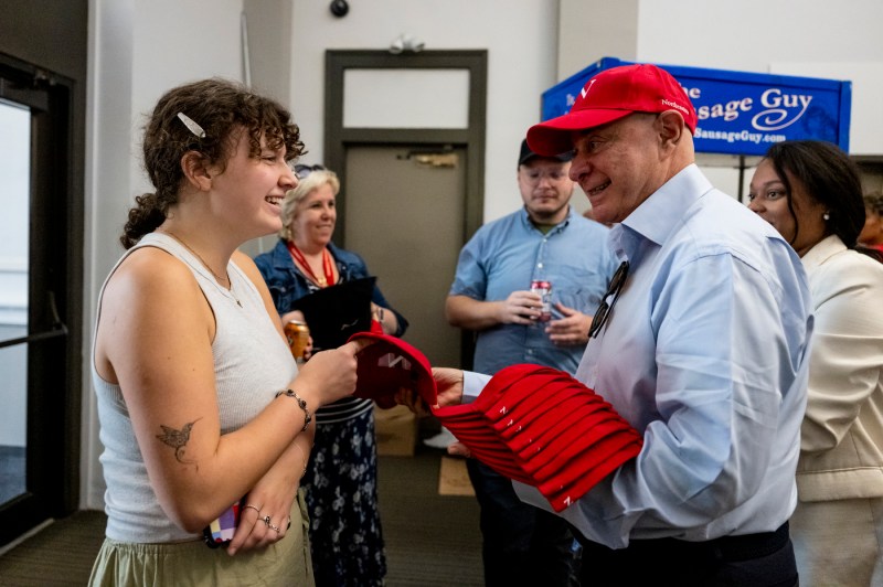 President Aoun handing out red hats to a person at the facillities BBQ. 