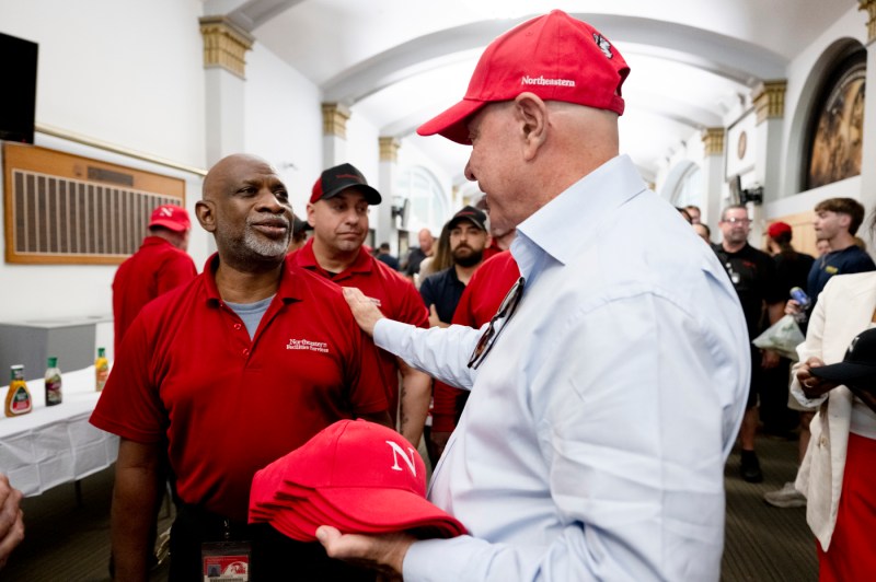 President Aoun wearing a red baseball cap putting his hand on the shoulder of a person at the facilities BBQ. 