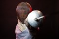 A person in fencing gear posing with their sword pointed at the camera.