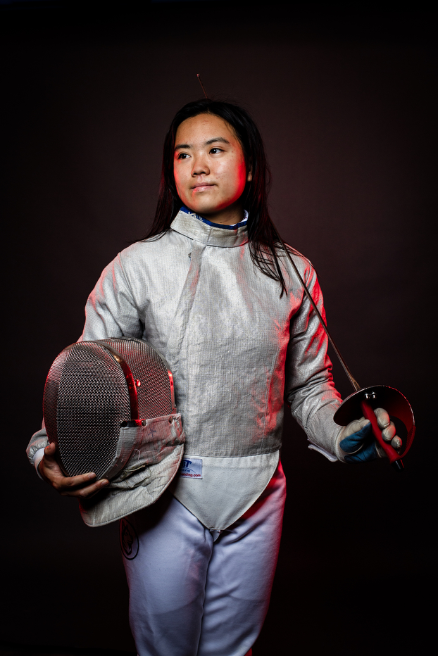 Laura Chu posing in fencing gear with a sword balanced over her shoulder.