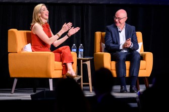 Claire Goldsmith (left) and President Aoun (right) sitting in orange chairs on the same stage. Claire is speaking and gesturing with her hands.