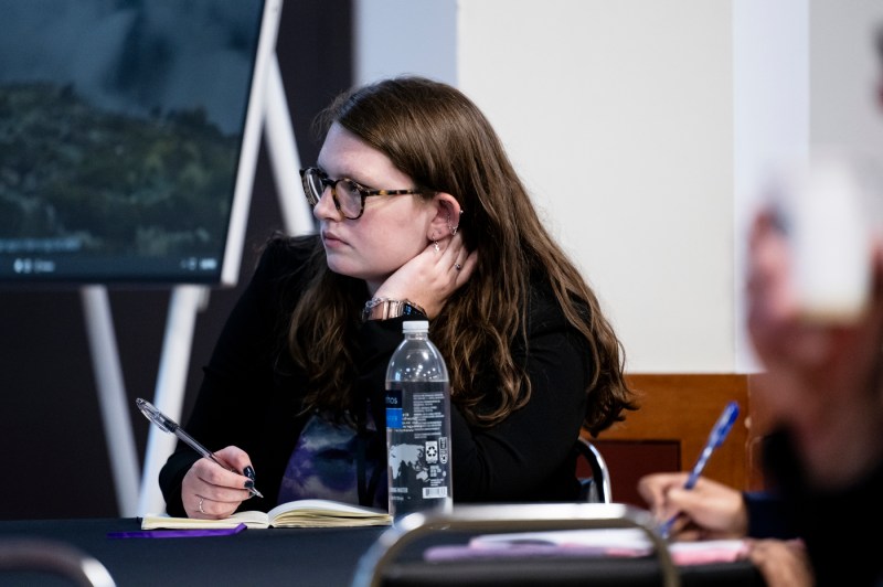 A student puts his hand on his neck while taking notes at a symposium.