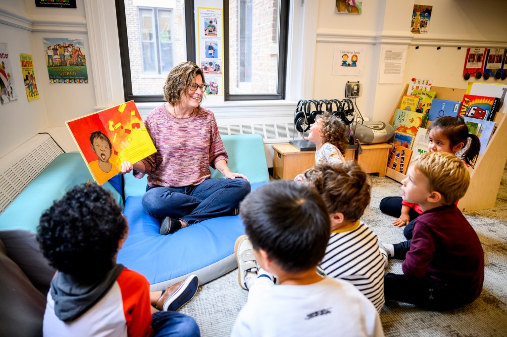 Lee Ann Burdick reading a kids book to a circle of children sitting around her.